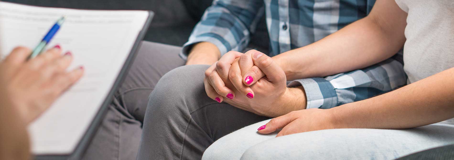 A couple holding hands in a therapy session with a therapist.
